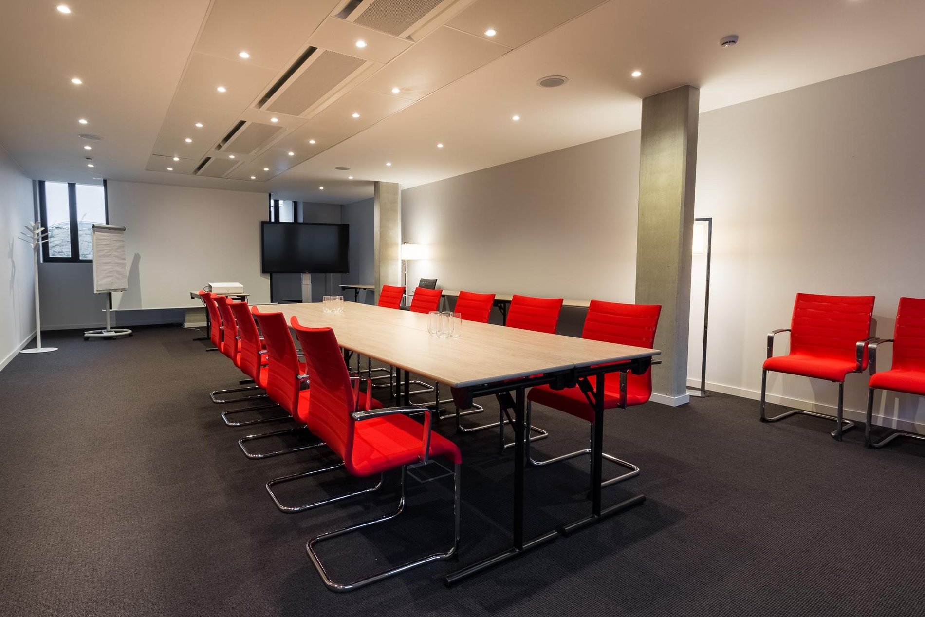 Moderne vergaderzaal met een grote rode tafel, zwarte stoelen en natuurlijk licht.