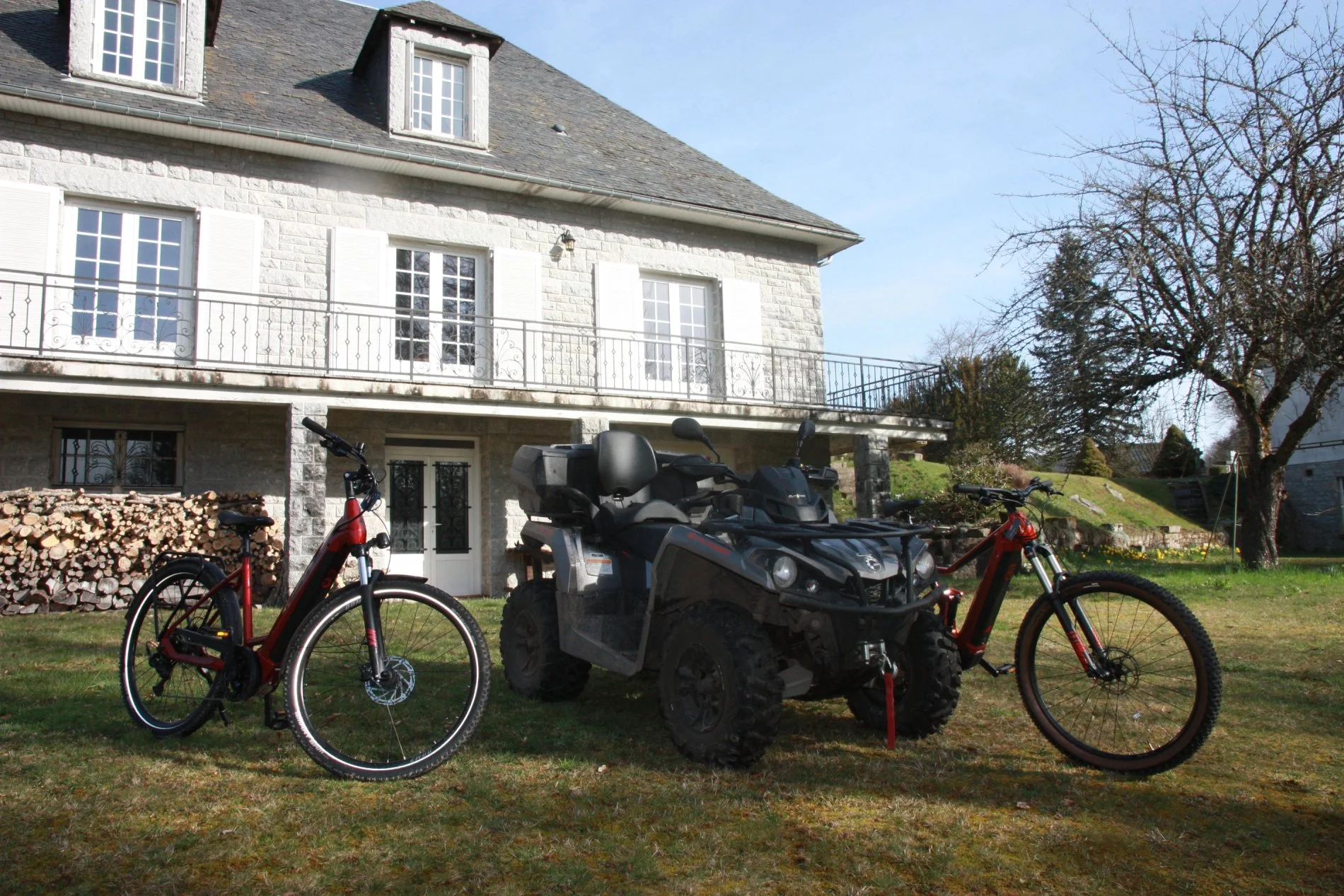 Deux vélos et un quad garés devant la façade principale de Villa Corrèze Aventure.