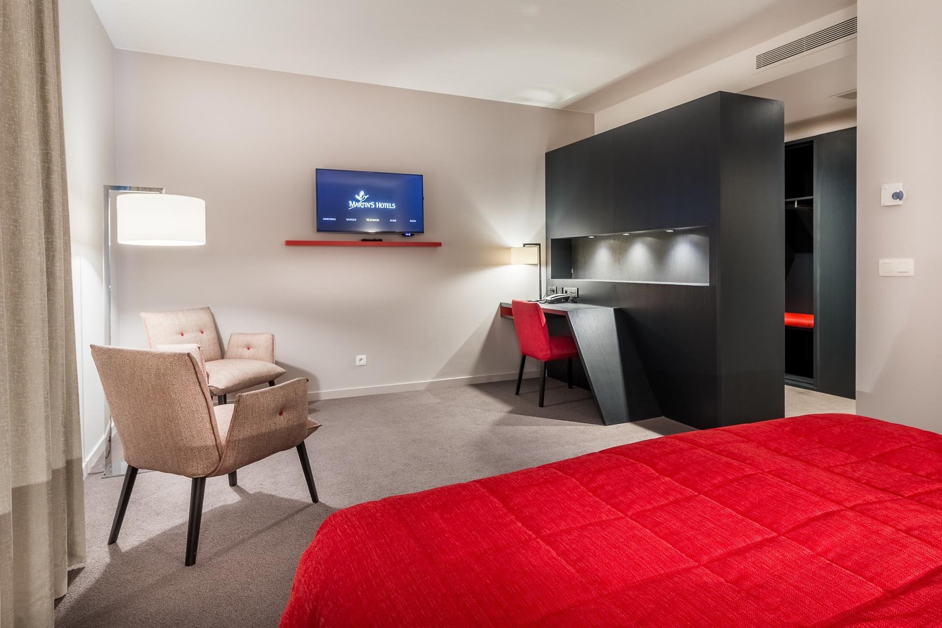 Spacious room at Martin's Red with a double bed, seating area, and wall-mounted TV.