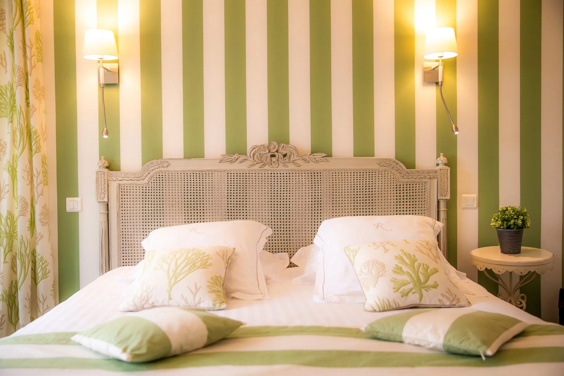 Tête de lit en bois dans la chambre 'Ville de Ramade' de l'Hôtel La Ramade avec mur à rayures vertes, symbolisant le style frais et naturel.