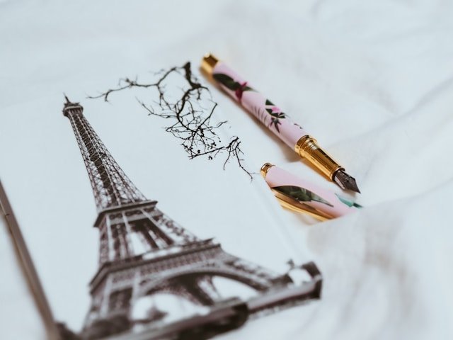 Carnet avec une illustration de la Tour Eiffel et un stylo plume rose et doré posé sur un drap blanc.
