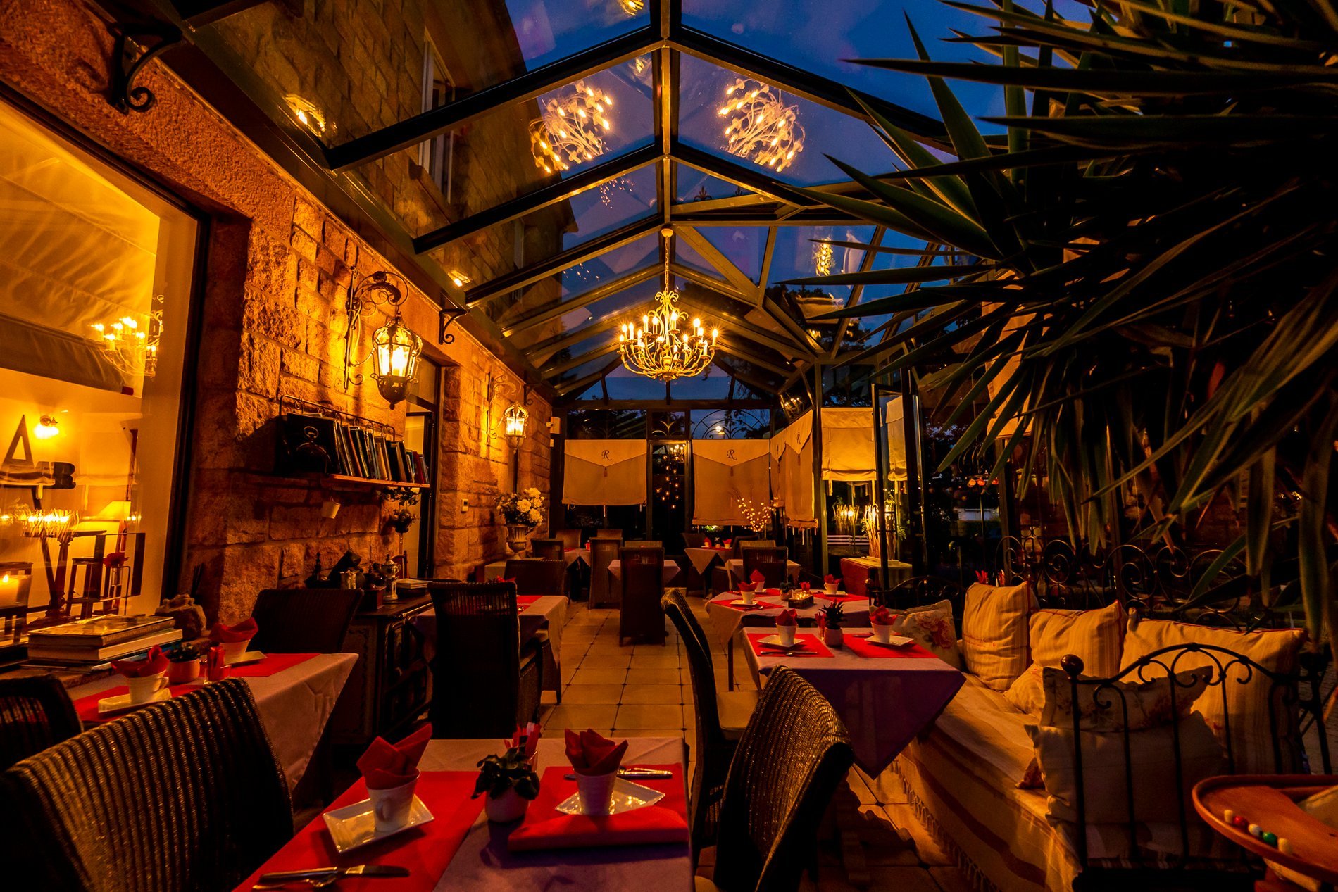 Interior of Hotel La Ramade's conservatory at night, lit and furnished, symbolizing an intimate dining or reception space.