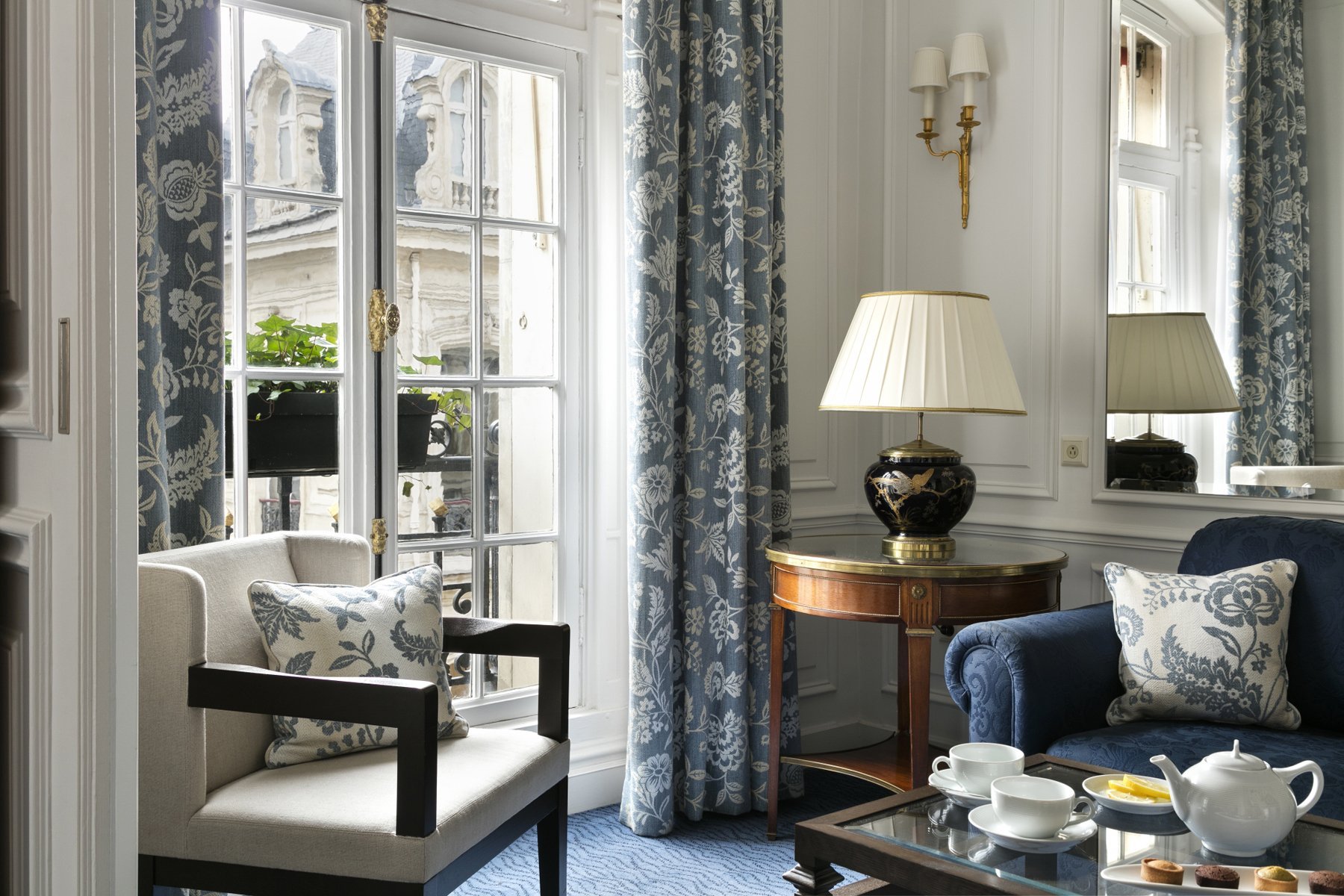 Salon raffiné avec vue sur Paris dans une Junior Suite de l’Hôtel San Régis, rideaux et mobilier assortis.