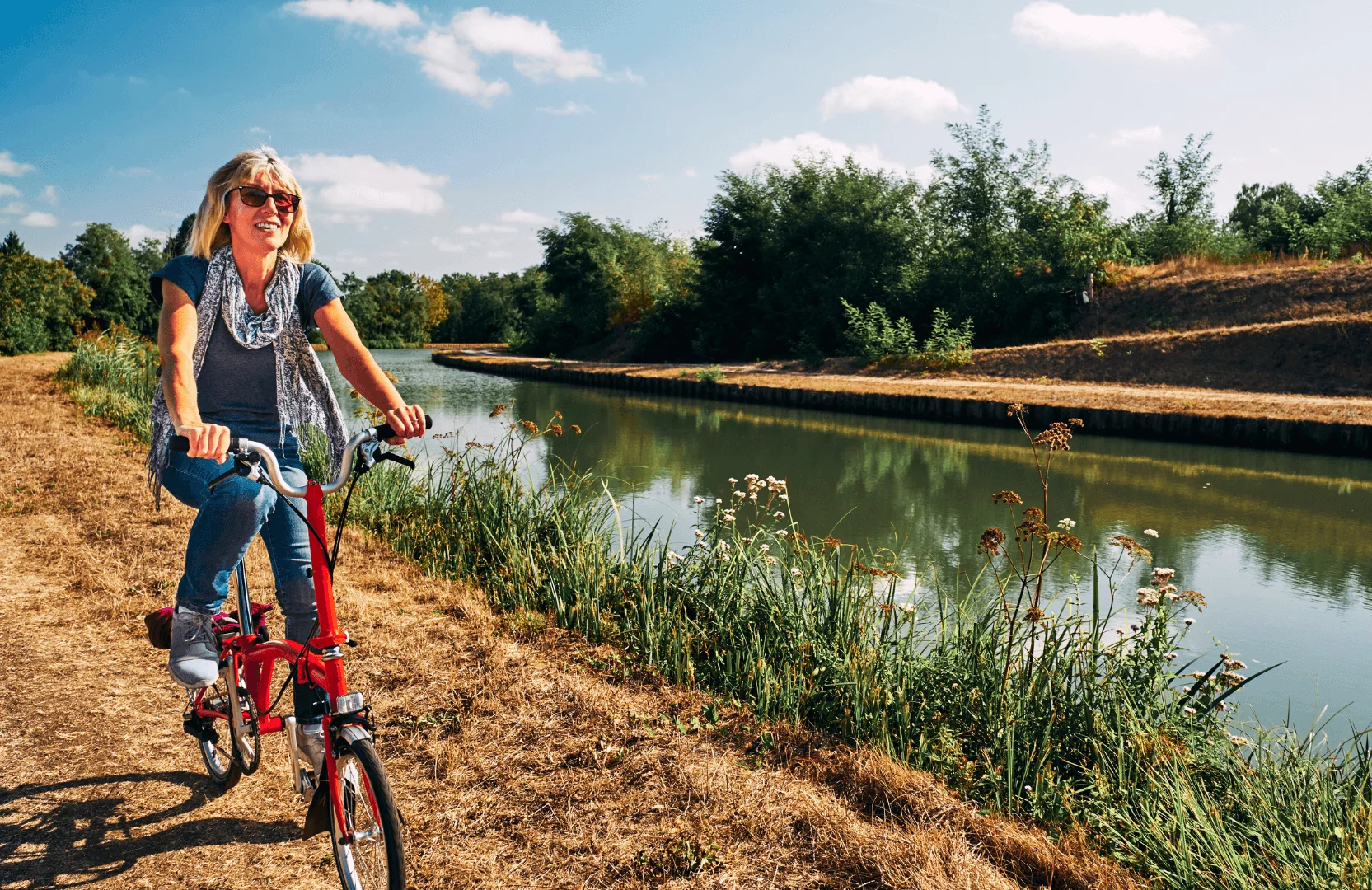 Femme souriante faisant du vélo le long d'un canal par une journée ensoleillée à Chenonceaux.