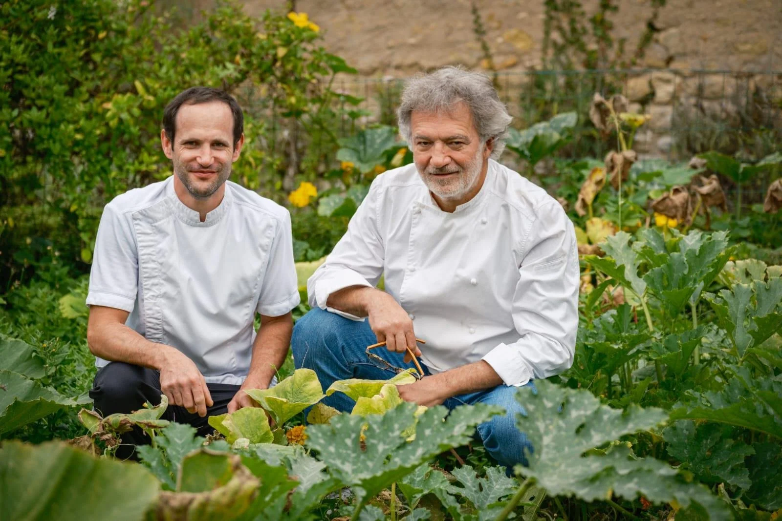 Deux chefs en tenue blanche dans un jardin potager.