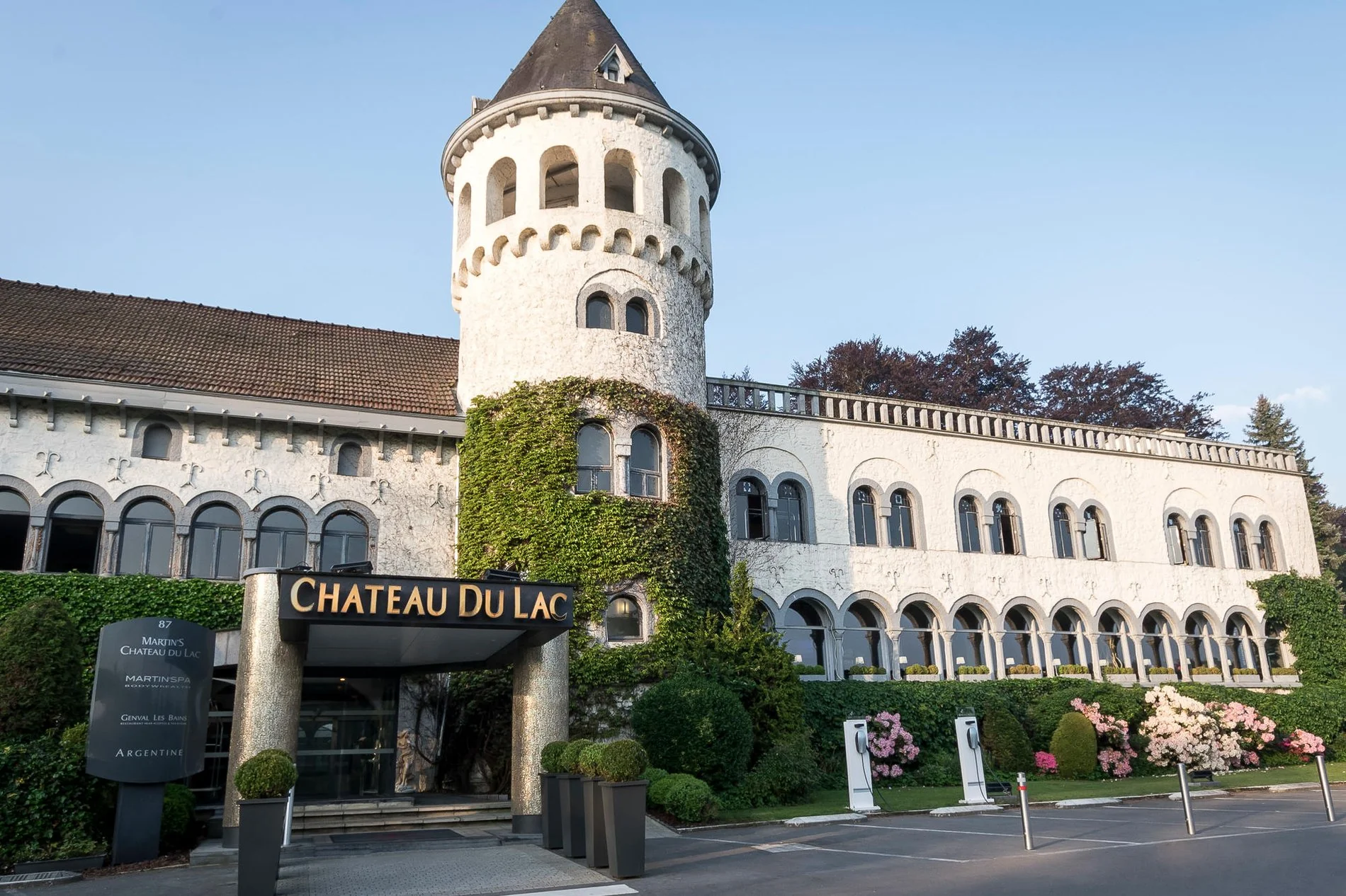 Façade principale du Martin's Château du Lac avec tour emblématique et verdure environnante.