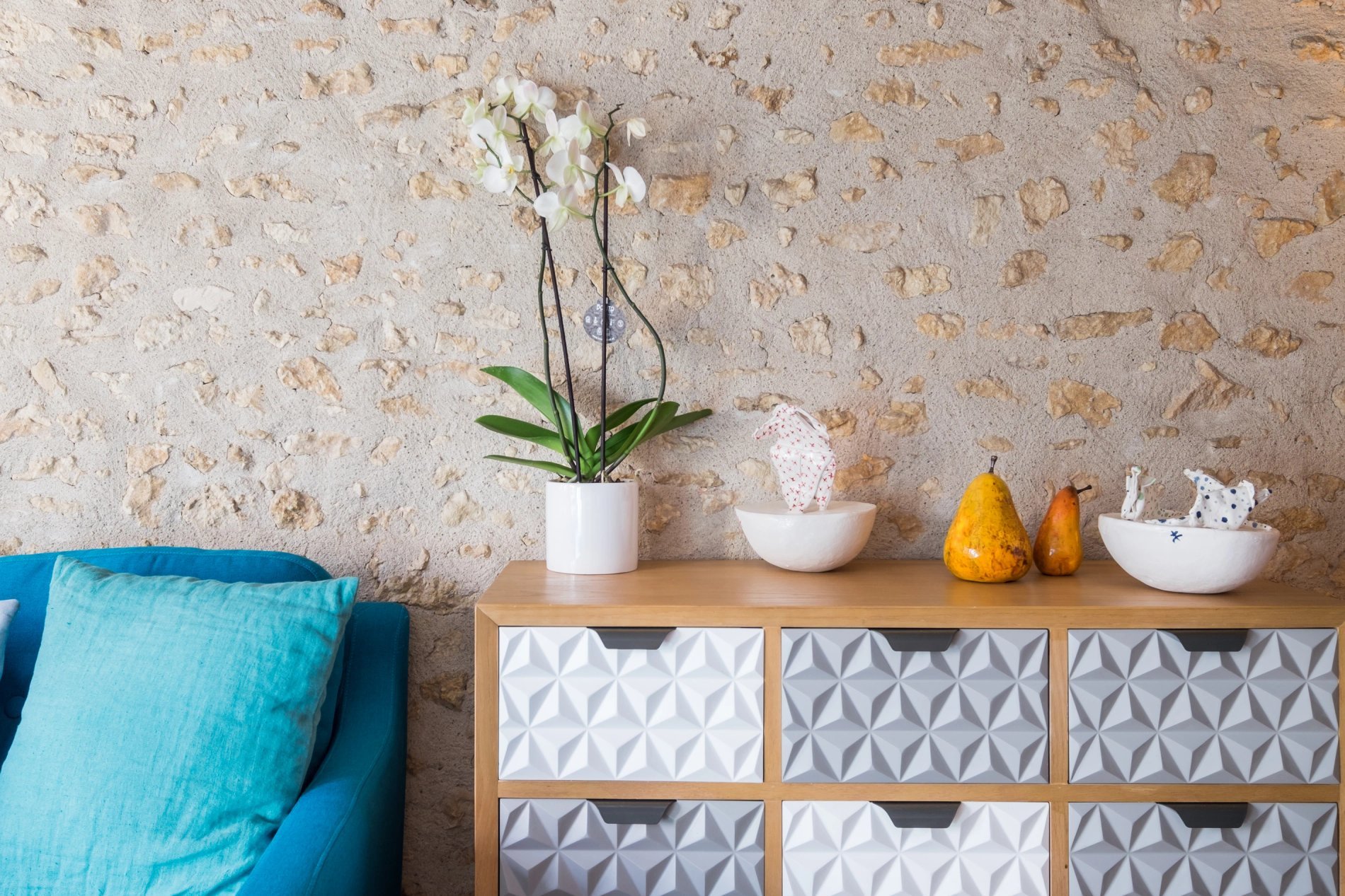 Intérieur avec un canapé bleu, une orchidée sur un meuble et un mur en pierre.