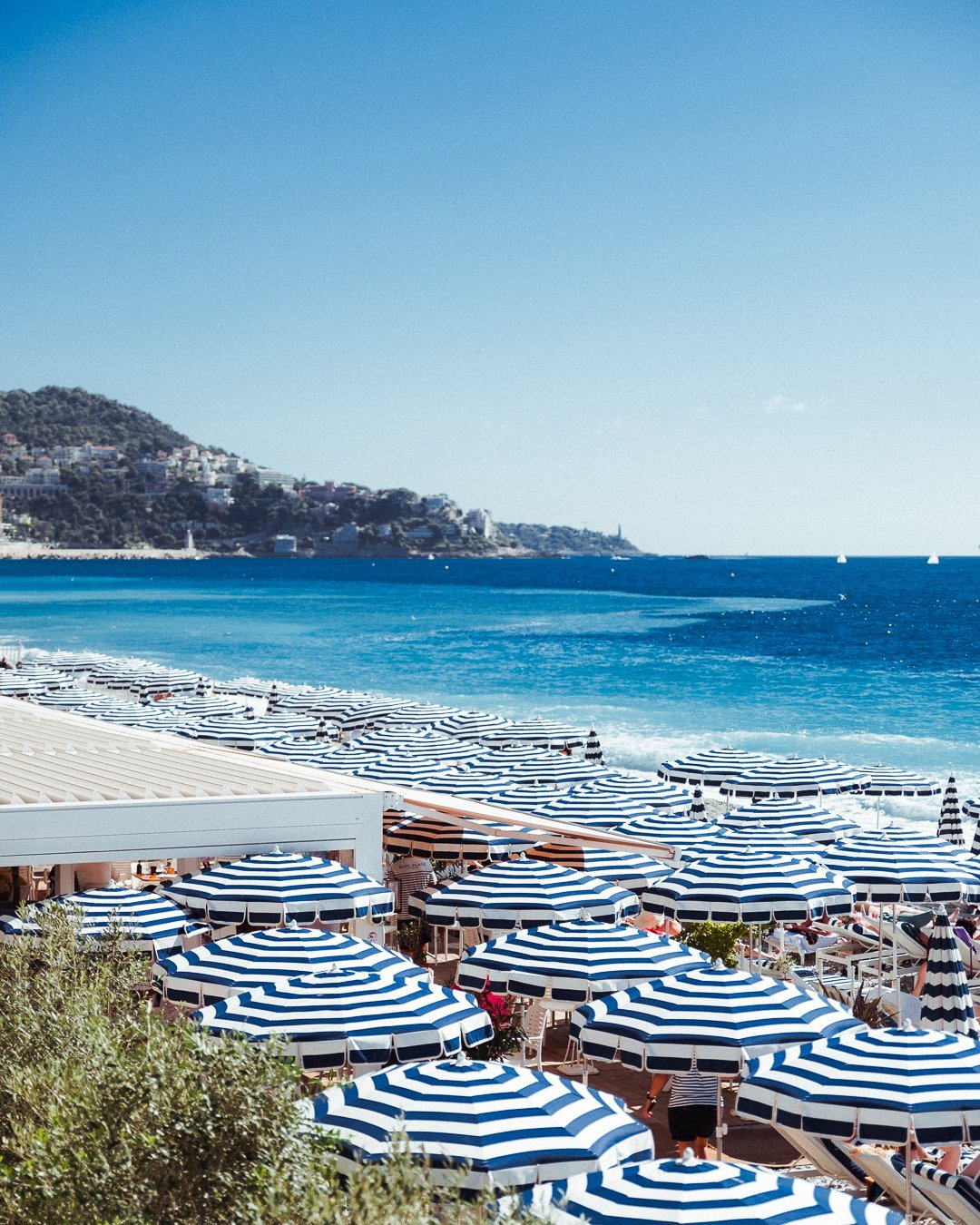 Maison Albar Le Victoria | Rangée de parasols bleus et blancs sur la plage de Nice.