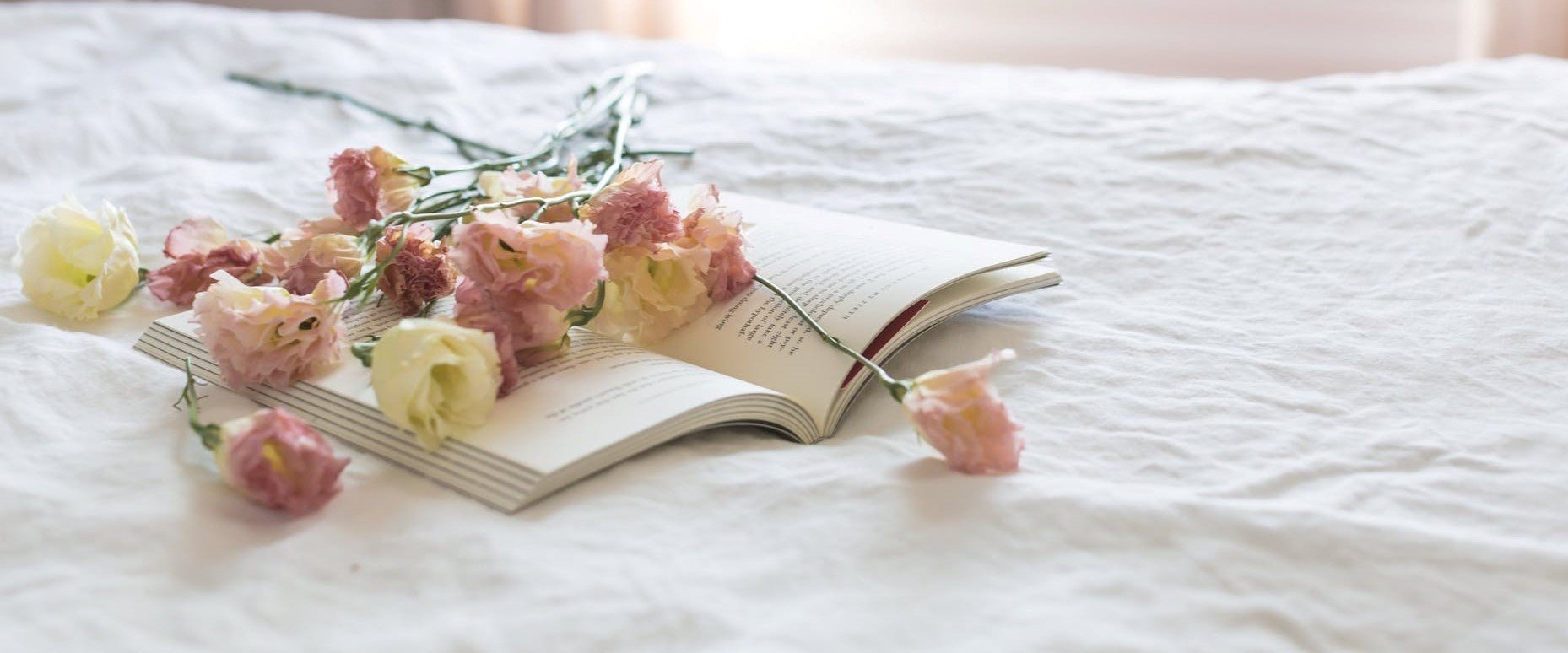 Fleurs pastel et livre ouvert sur un tissu clair, symbolisant la détente et l'ambiance cosy de BW La Demeure Paris.