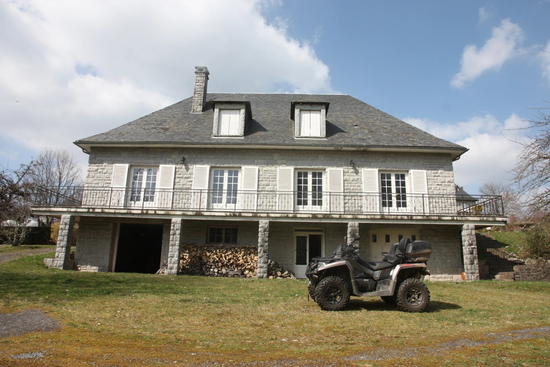 Façade principale de Villa Corrèze Aventure avec volets blancs, bûches empilées et quad garé devant.
