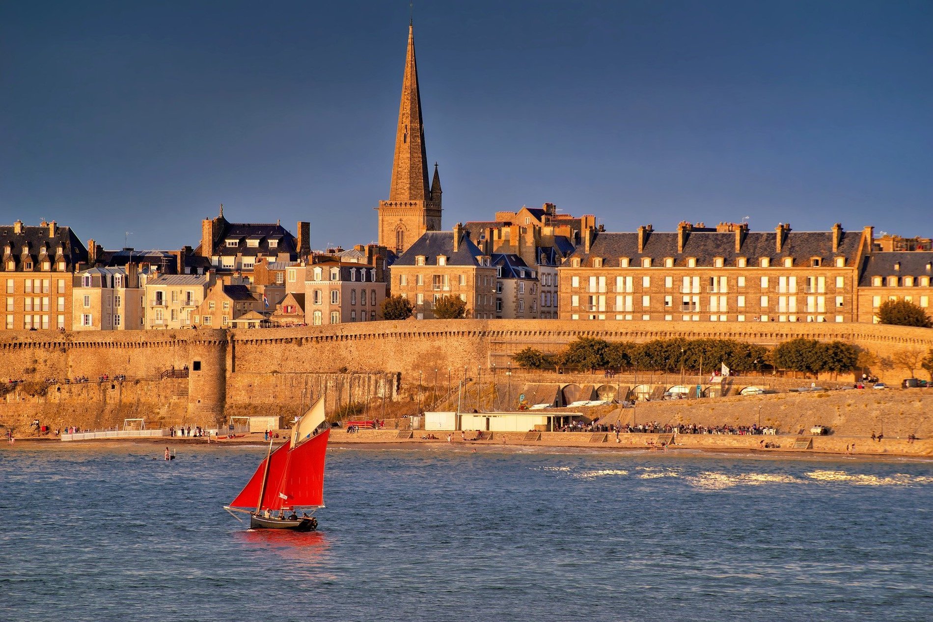 Fortified coastal town with a sailboat at sea, symbolizing the attractions of the Normandy and Brittany coastlines.