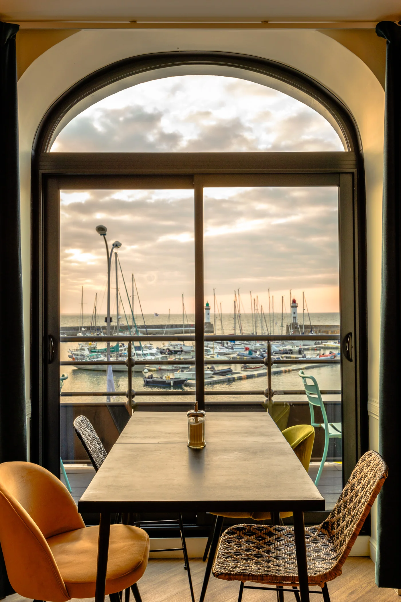 Salle de restaurant avec vue sur le port du Palais à Belle-Île-en-Mer à travers une grande fenêtre cintrée